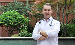 Dr. Brian Greenwell stands outside in a garden with a stethoscope around his neck